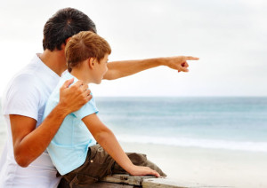 C4P591 Father and son on a beach vacation together, father pointing towards the sea